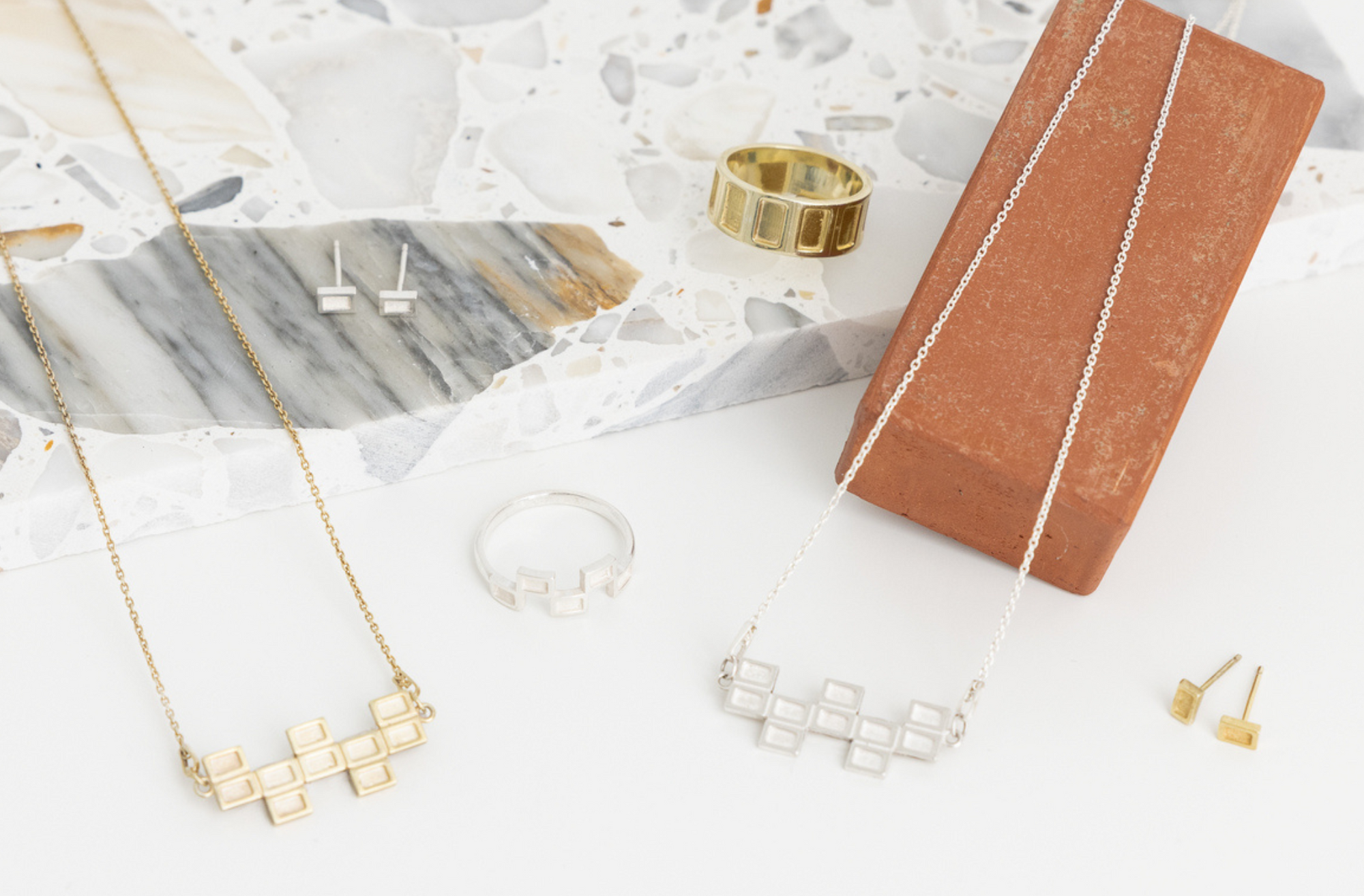 A selection from the Concrete Waffles Collection, featuring jewelry inspired by the architectural elements of the Washington D.C. Metro, arranged on a terrazzo slab with a brick backdrop.