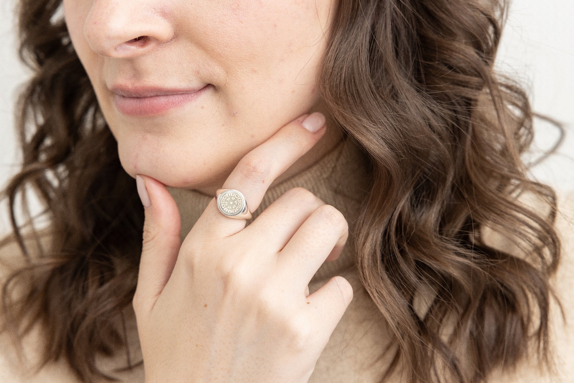 A side view of a smiling woman with wavy hair, touching her chin with a hand featuring a 12mm silver Manhattan Mini Manhole signet ring.